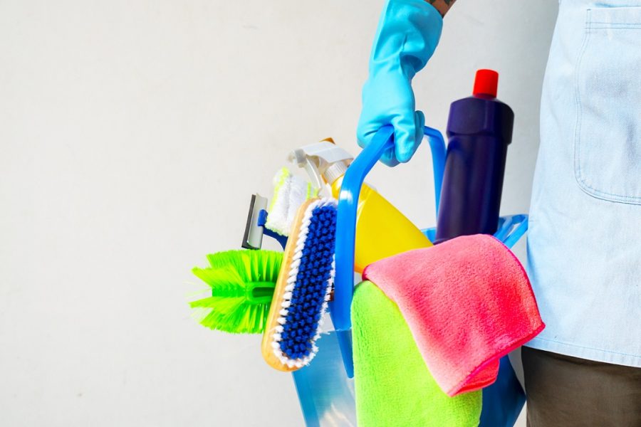 Man holding mop and plastic bucket with brushes, gloves and detergents in the kitchen