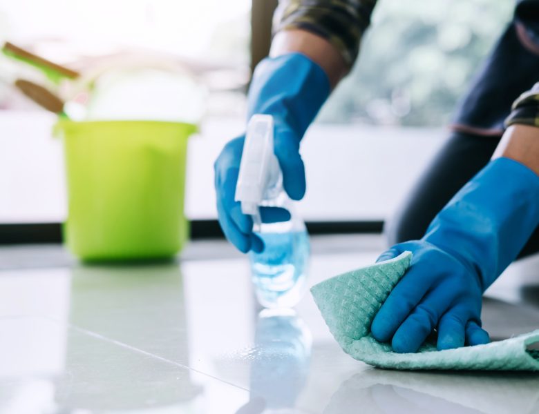 Husband housekeeping and cleaning concept, Happy young man in blue rubber gloves wiping dust using a spray and a duster while cleaning on floor at home.